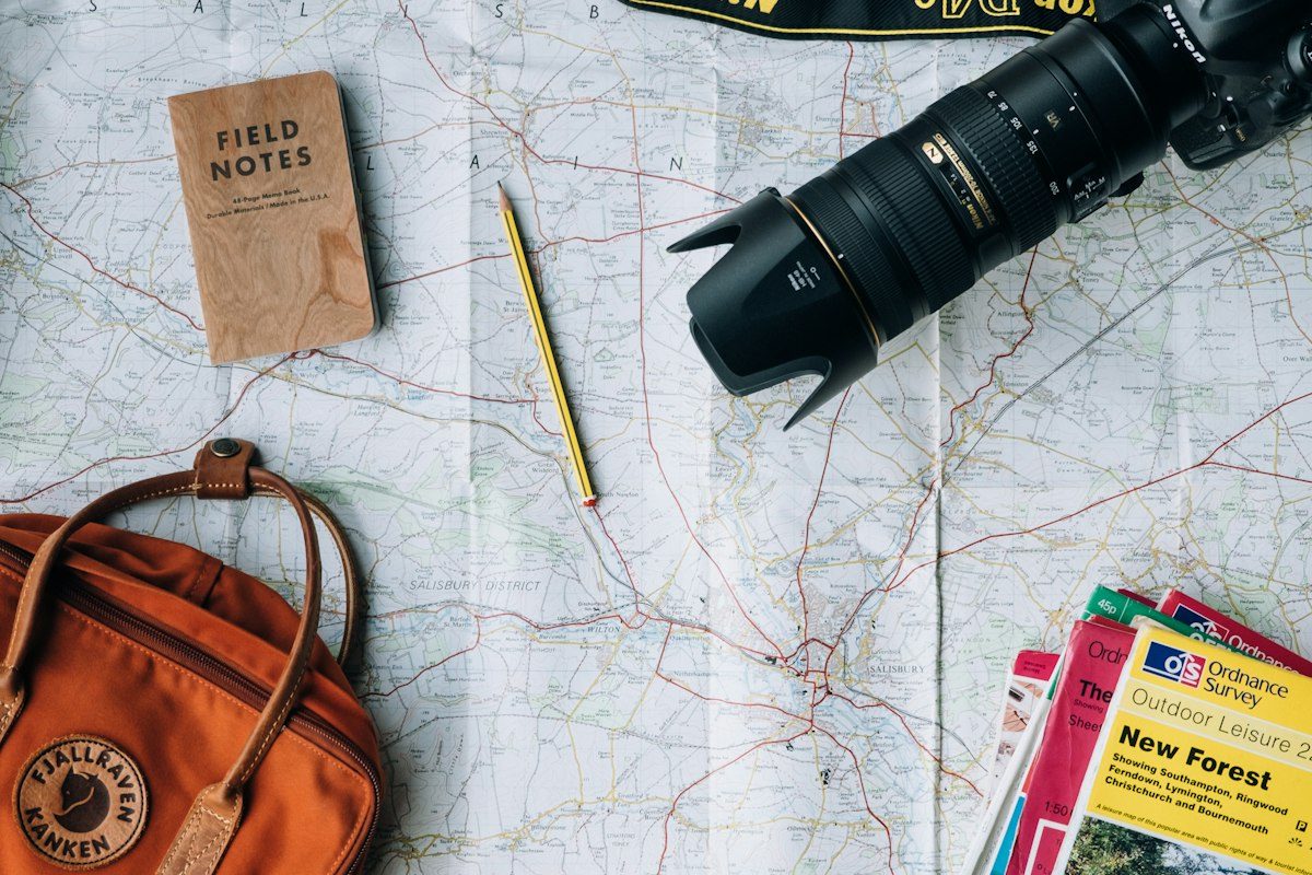 A map spread out with a camera, field notes, a pencil and a backpack